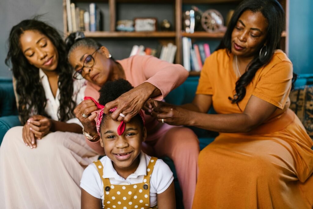 Three generations of women sharing a tender moment while fixing a young girl's hair in a cozy living room.